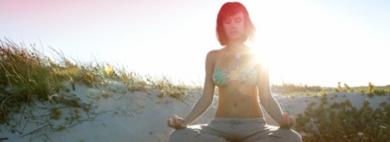 Foto di una donna seduta in meditazione sulla spiaggia. L’immagine illustra che è possibile rilassarsi e vivere normalmente anche durante il ciclo.