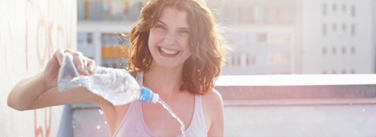 Foto di una giovane donna con in mano una bottiglietta da cui versa dell’acqua.